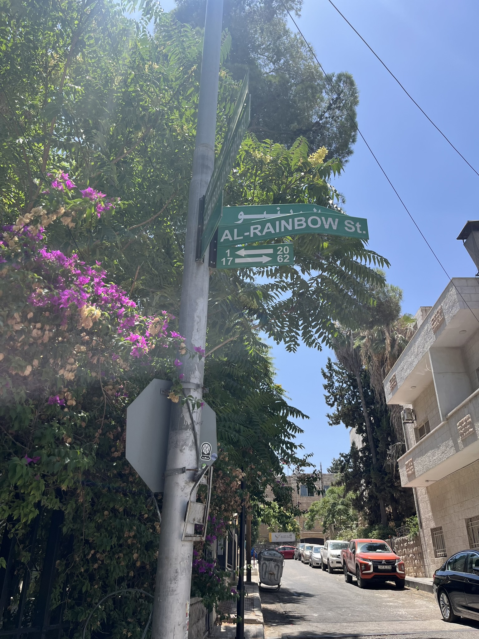 AL-RAINBOW St. street sign on a pole with bougainvillea flowers and stone buildings in Jabal Amman